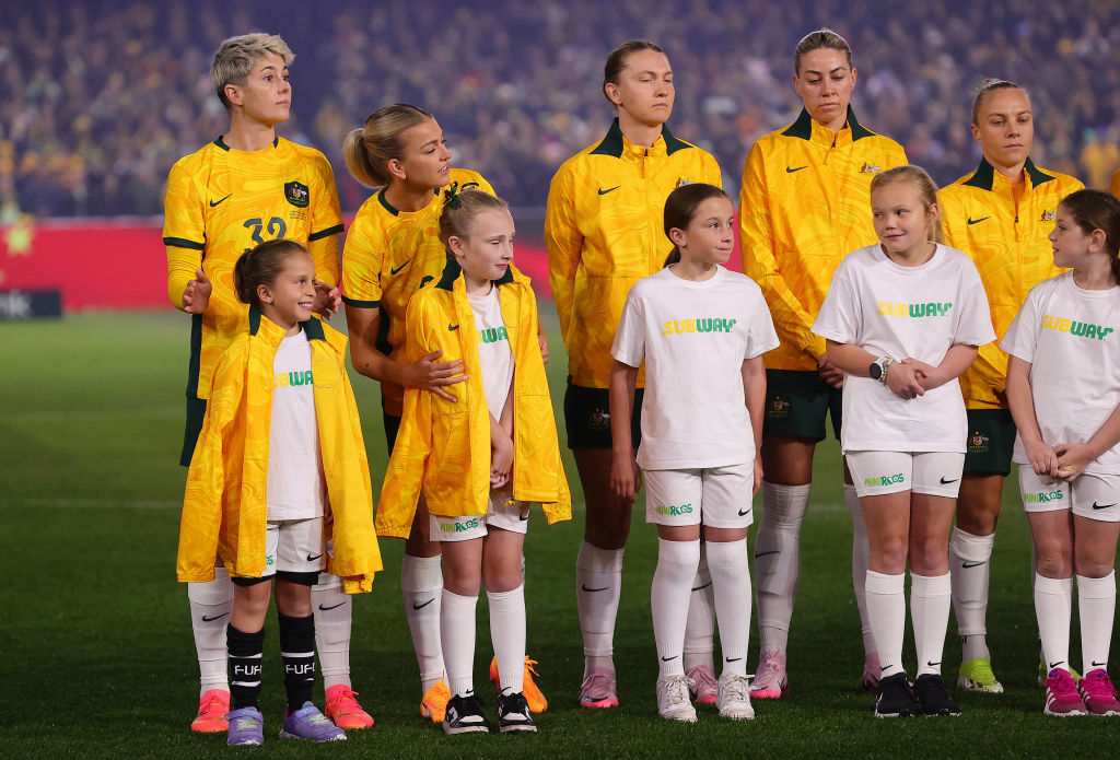 ADELAIDE, AUSTRALIA - MAY 31: Michelle Heyman of Australia and Charlotte Grant of Australia put their jackets around the mascots during the national anthem during the international friendly match between Australia Matildas and China PR at Adelaide Oval on May 31, 2024 in Adelaide, Australia. (Photo by Sarah Reed/Getty Images)